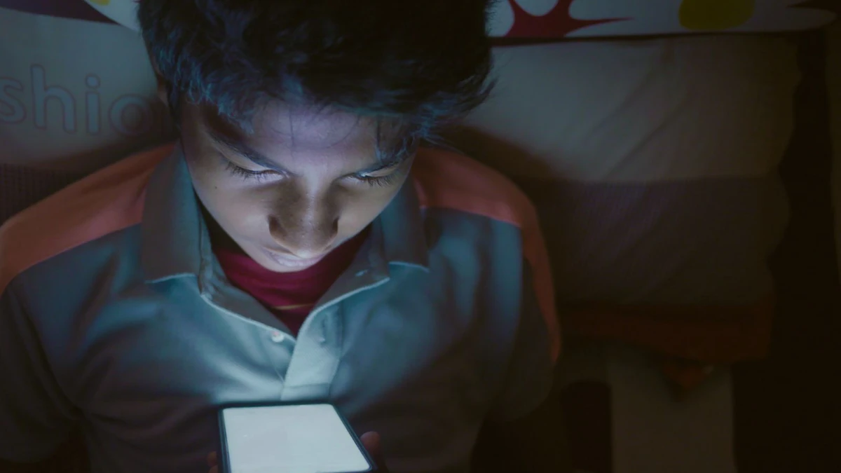 Menino deitado na cama à noite olhando atentamente para a tela acesa do celular, tema da suspensão das transmissões ao vivo do Discord após a morte de menina de 13 anos